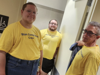 Three trans masculine activists with the Compliance Crew stand at the door of a public women's restroom.