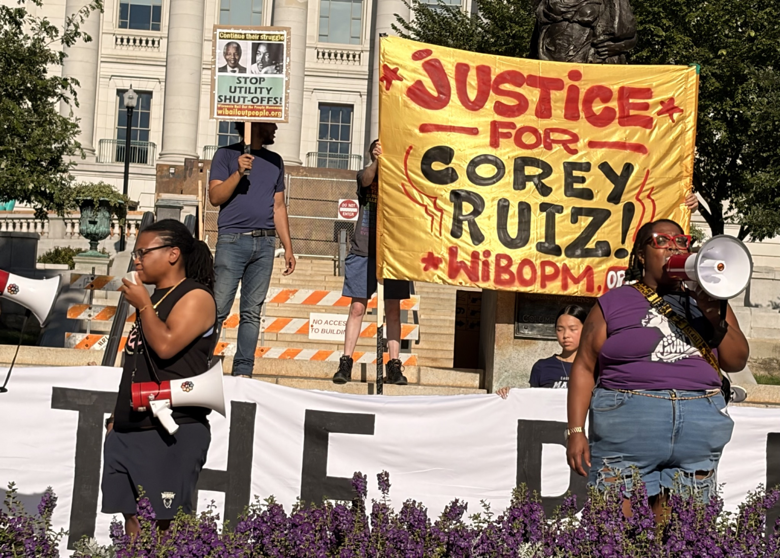 Two protesters in front of "Justice for Corey Ruiz" banner speak into megaphones.